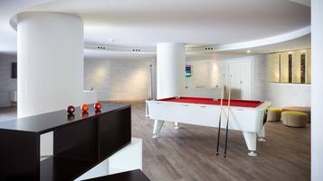 A modern pool table in a well-lit room with a minimalist design, featuring a white pool table, red felt, and a black pool cue rack.