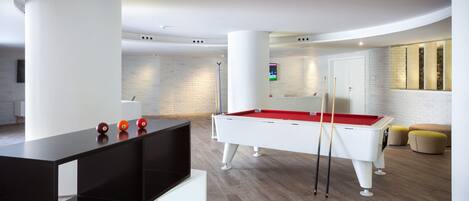 A modern pool table in a well-lit room with a minimalist design, featuring a white pool table, red felt, and a black pool cue rack.