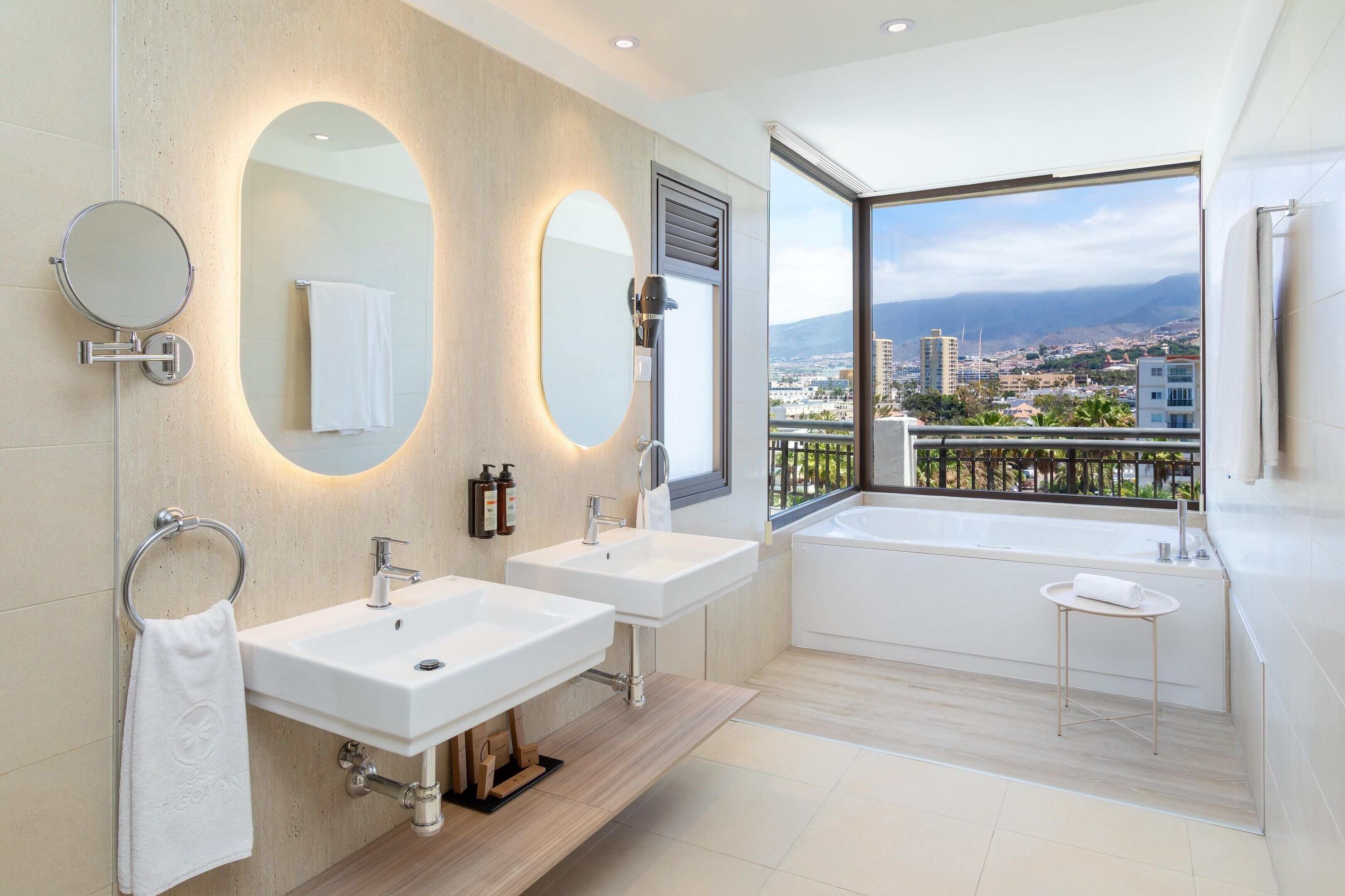 A modern bathroom with two sinks, a large mirror, and a bathtub.