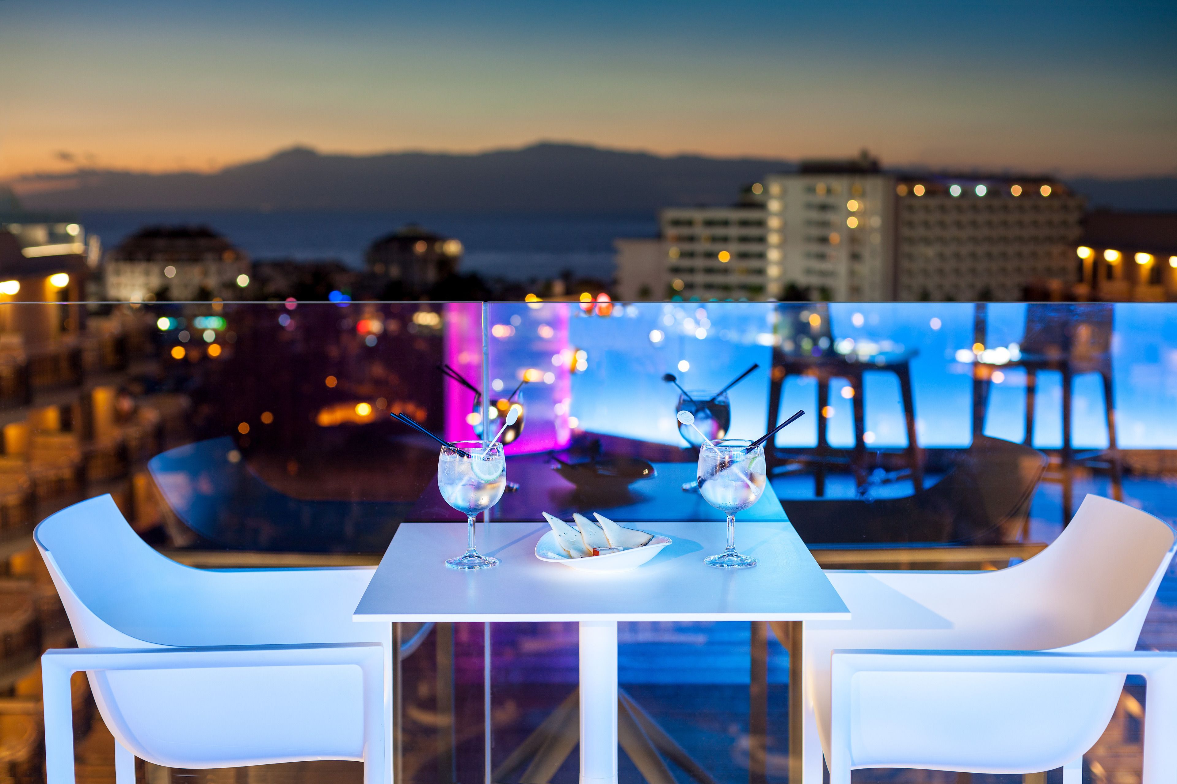 Una terraza en la azotea con mesa y sillas, con vistas a un paisaje urbano y montañas.