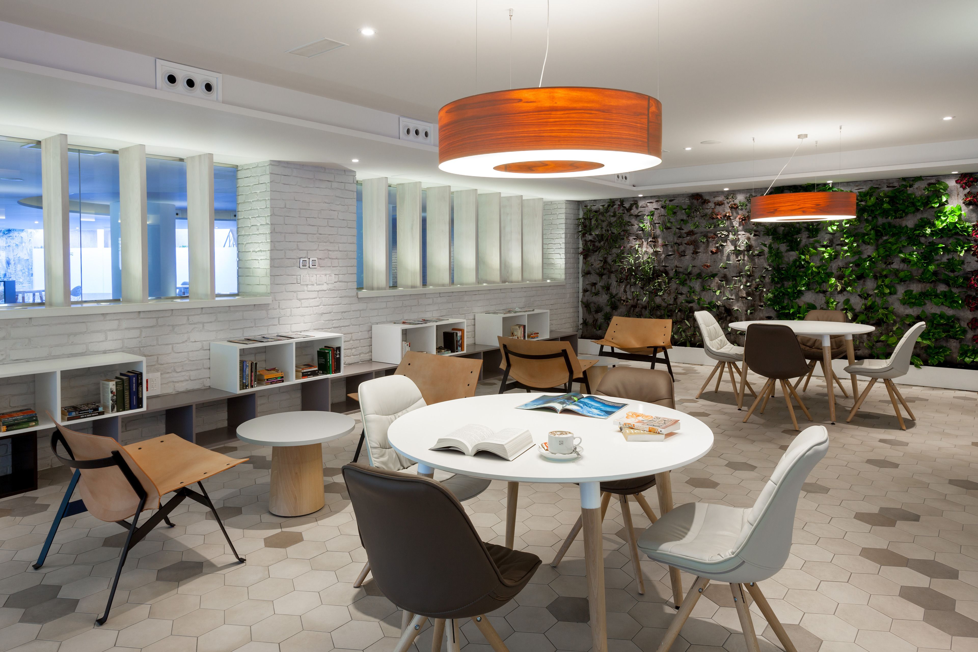 A modern interior with round tables and chairs, a white brick wall, and a green wall with plants.