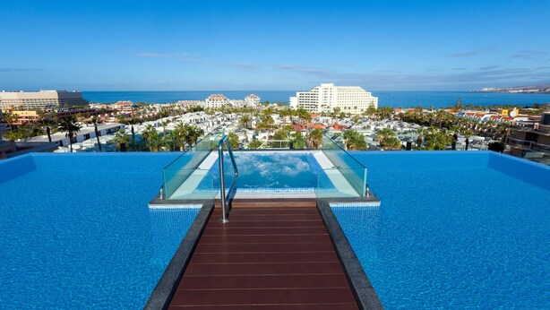 An infinity pool with a glass edge, leading to a beach view.