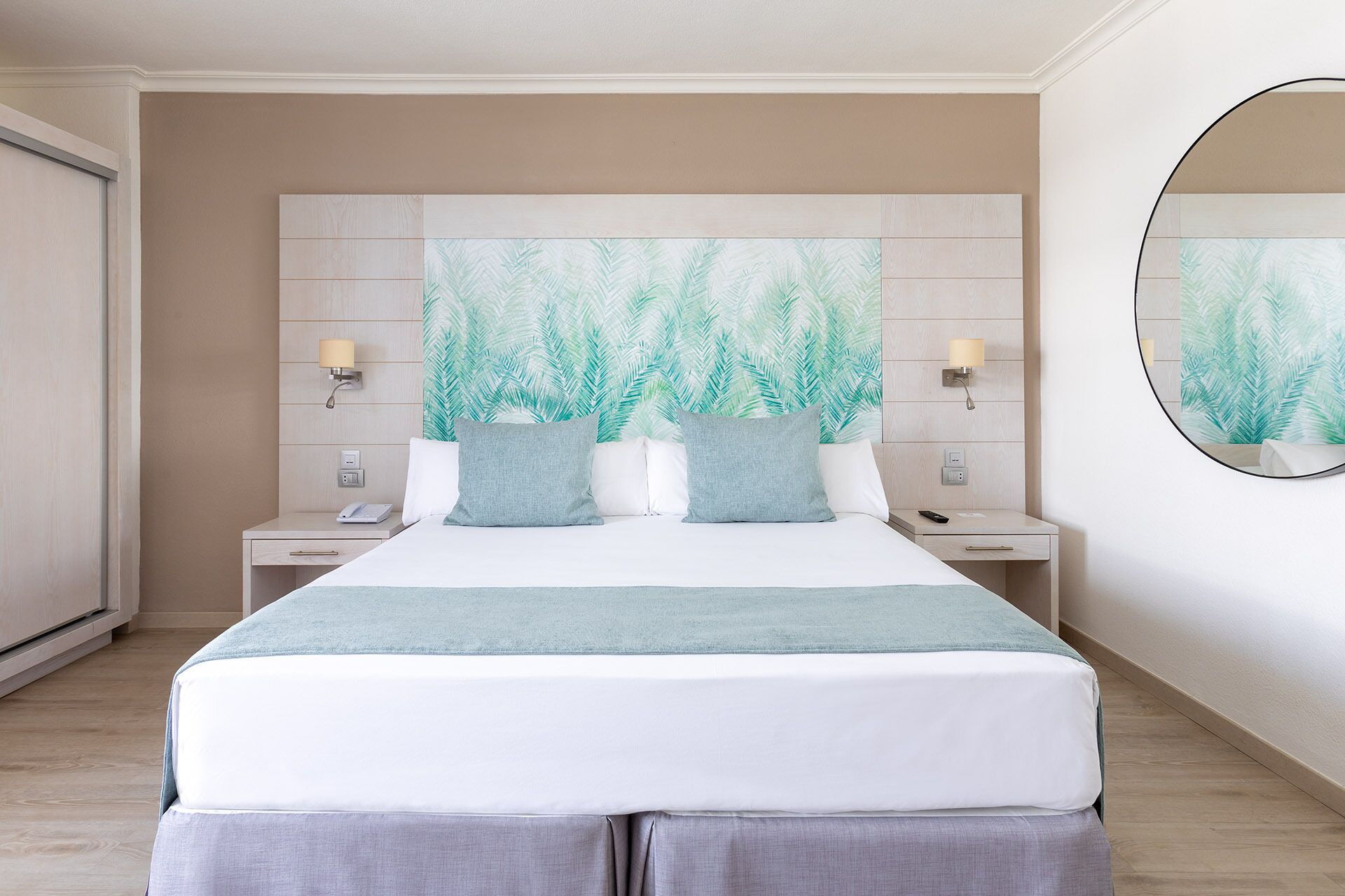 Una habitación de hotel con una cama, mesitas de noche, una lámpara de pared y un espejo grande.