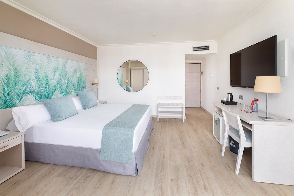 A hotel room with a bed, a desk, a chair, a TV, and a large mirror.