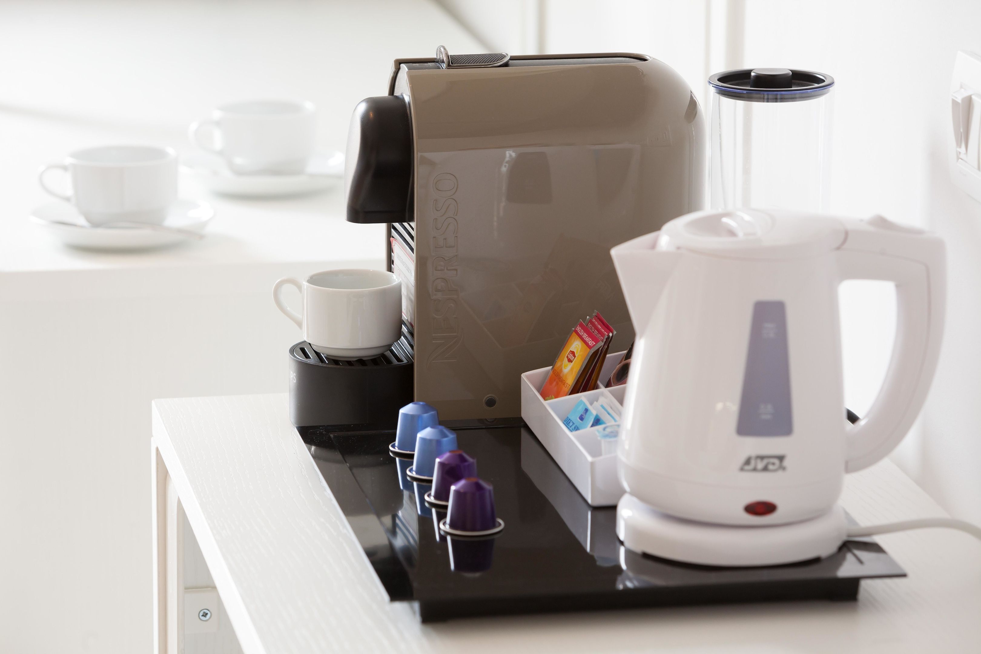 A coffee machine, a kettle, and a cup of coffee on a tray.