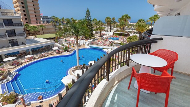 A pool area with a view of the ocean, red chairs, and a building in the background. - Tigotan Lovers & Friends Playa de las Américas - Adults Only (+18) (Arona)
