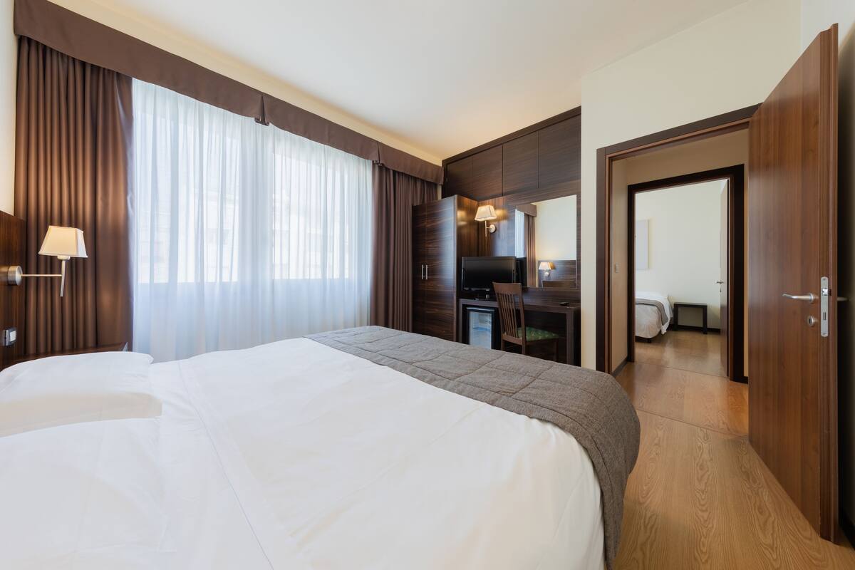 A hotel room with a large bed, a desk with a chair, a television, and a bathroom visible through an open door.