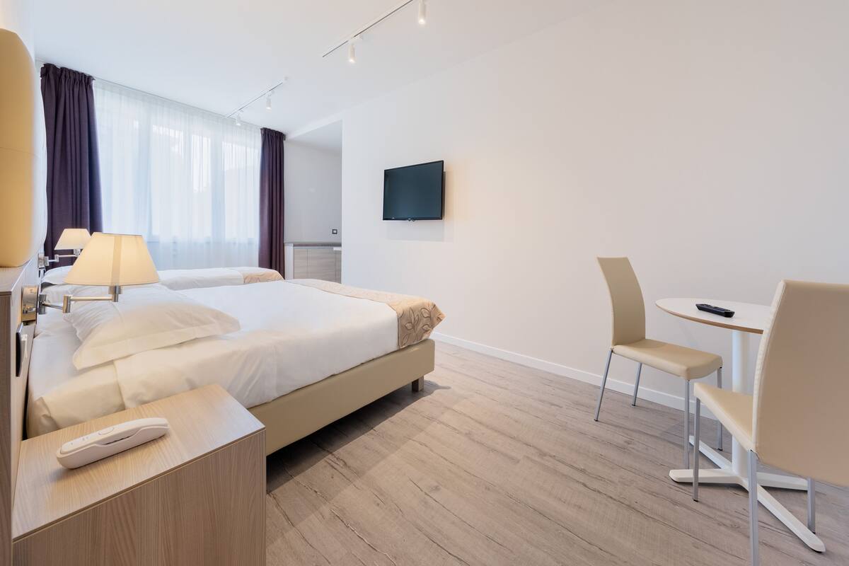 A hotel room with a bed, bedside tables, a TV, and a small dining area with chairs.