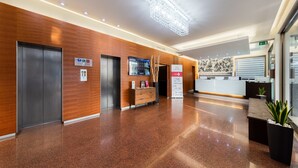 A modern hotel lobby with a reception desk, elevators, and a digital directory. - Hotel Delfino (Mestre)
