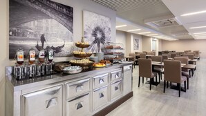 A modern hotel lobby with a buffet area featuring a variety of food items and a large black and white mural of a bridge. - Hotel Delfino (Mestre)
