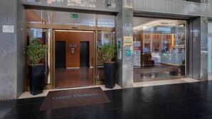 A hotel entrance with a modern design, including a reception desk, glass doors, and potted plants. - Hotel Delfino (Mestre)