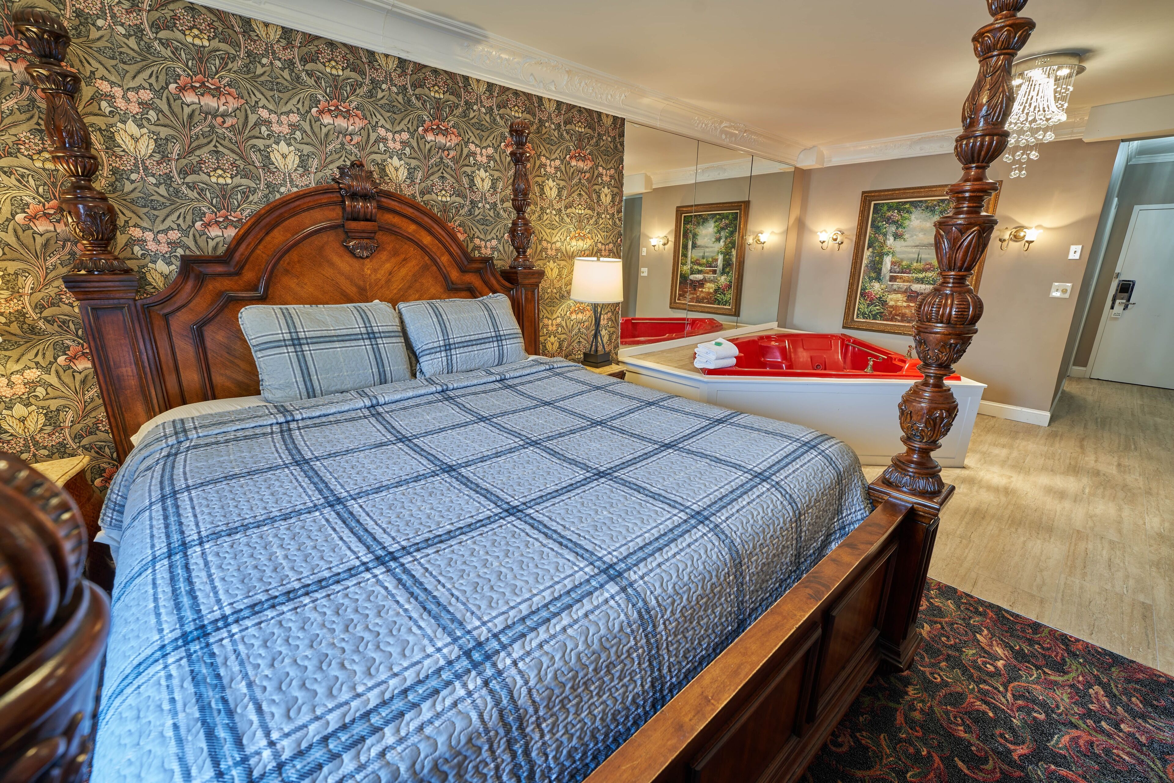 Una cama con dosel con colcha escocesa, una bañera roja y un papel pintado con motivos florales.