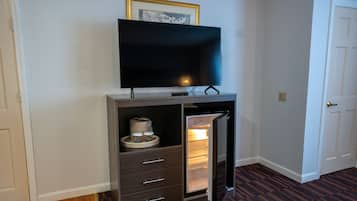 Un espacio habitable compacto con una televisión integrada en un mueble de madera, un refrigerador pequeño y una puerta que da a otra habitación.