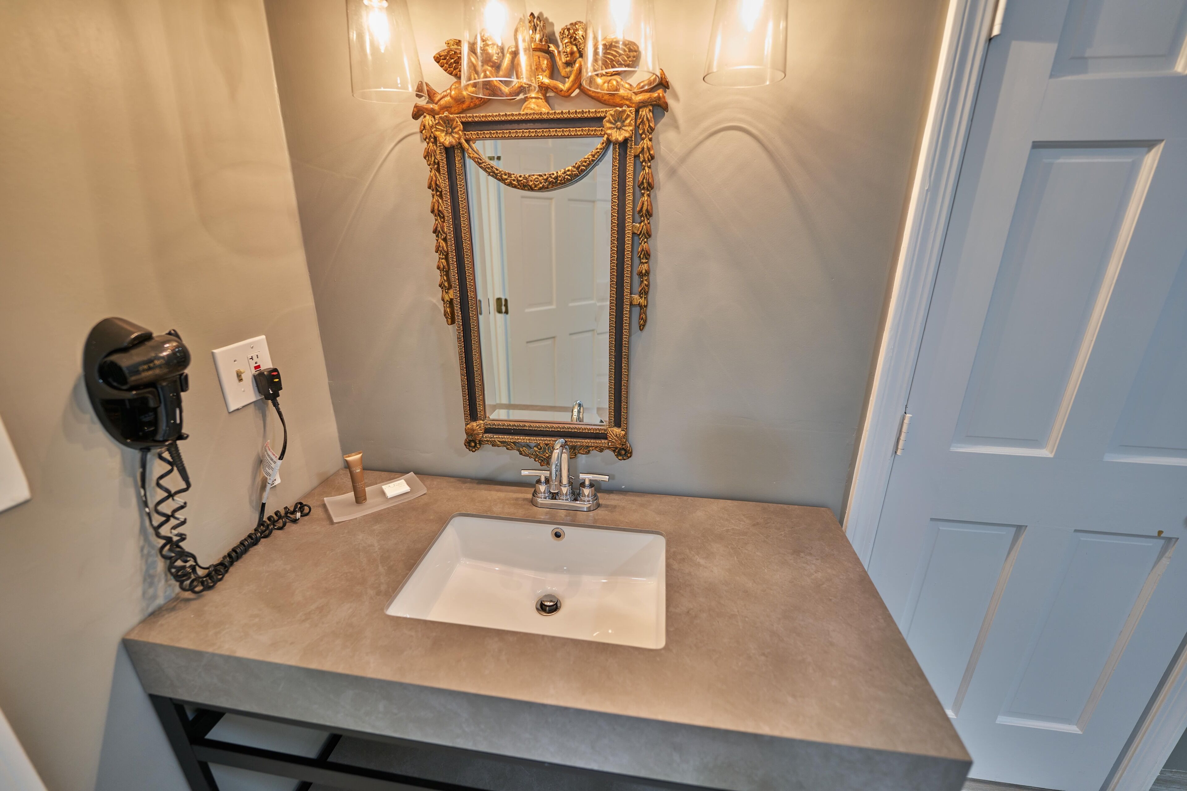 A bathroom with a white sink, gold-framed mirror, and a hairdryer on the wall.