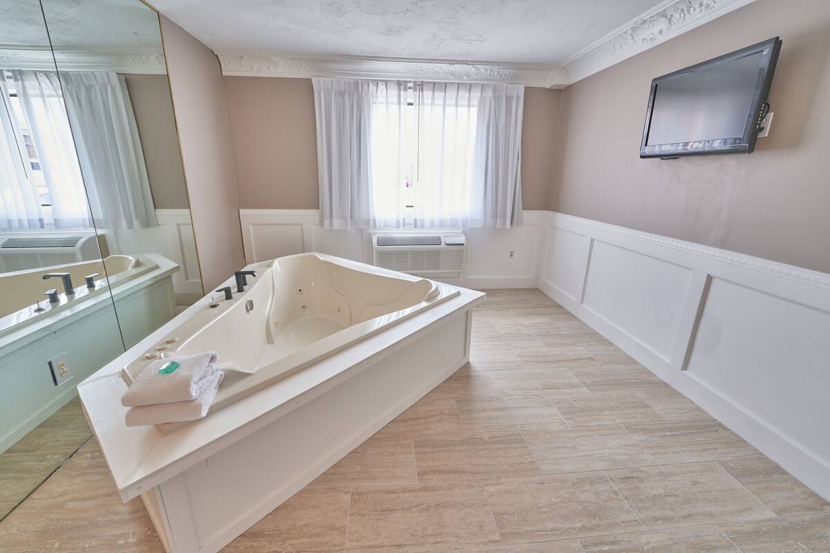 Une salle de bain moderne avec une grande baignoire, un meuble-lavabo avec un miroir et un téléviseur fixé au mur.
