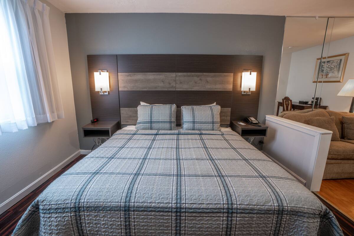 Une chambre d’hôtel avec un grand lit, deux tables de chevet avec des lampes, une table de nuit, une chaise et un bureau avec une lampe.