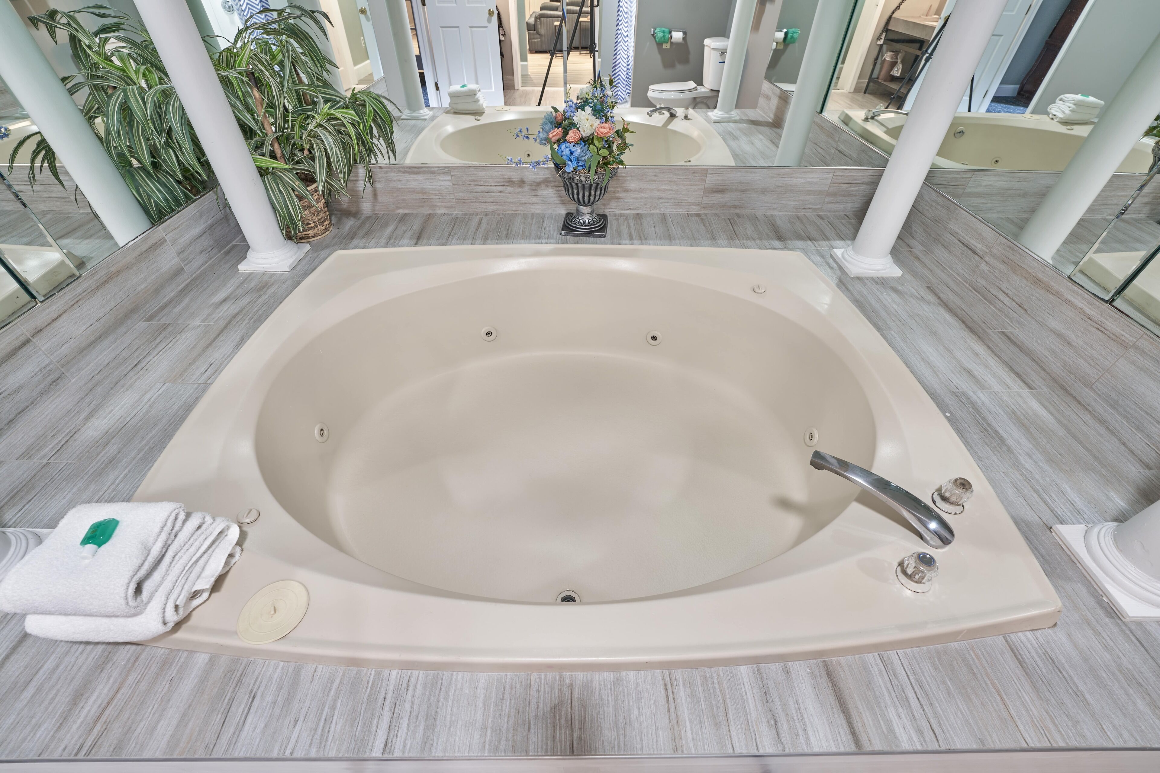 Una bañera grande con un arreglo floral, una toalla y un jabonera en un baño moderno con suelo de baldosas y paredes de vidrio.