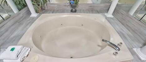 Una bañera grande con un arreglo floral, una toalla y un jabonera en un baño moderno con suelo de baldosas y paredes de vidrio.