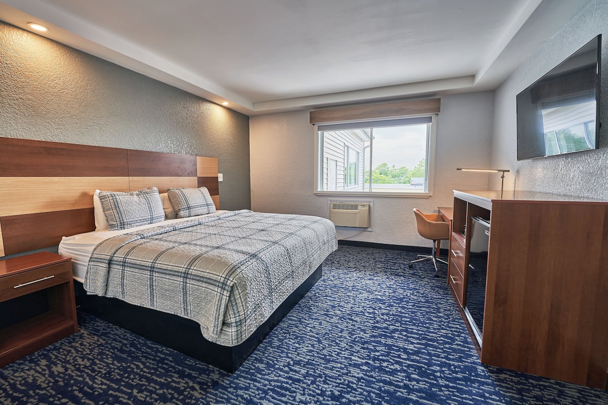 Une chambre d’hôtel avec un grand lit, un bureau, une chaise et un téléviseur fixé au mur.