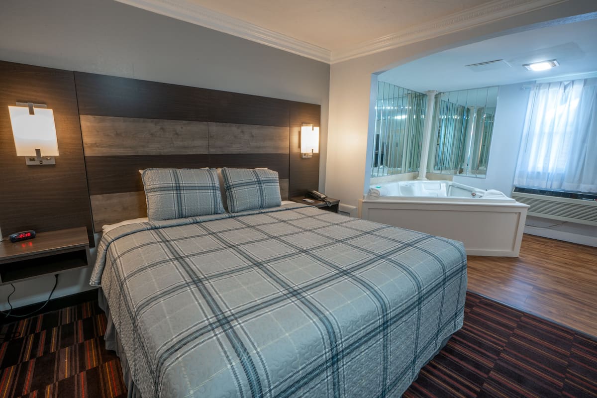 Une chambre d’hôtel avec un grand lit, une table de chevet avec une lampe, un téléphone et une salle de bain équipée d’une baignoire et d’un miroir.