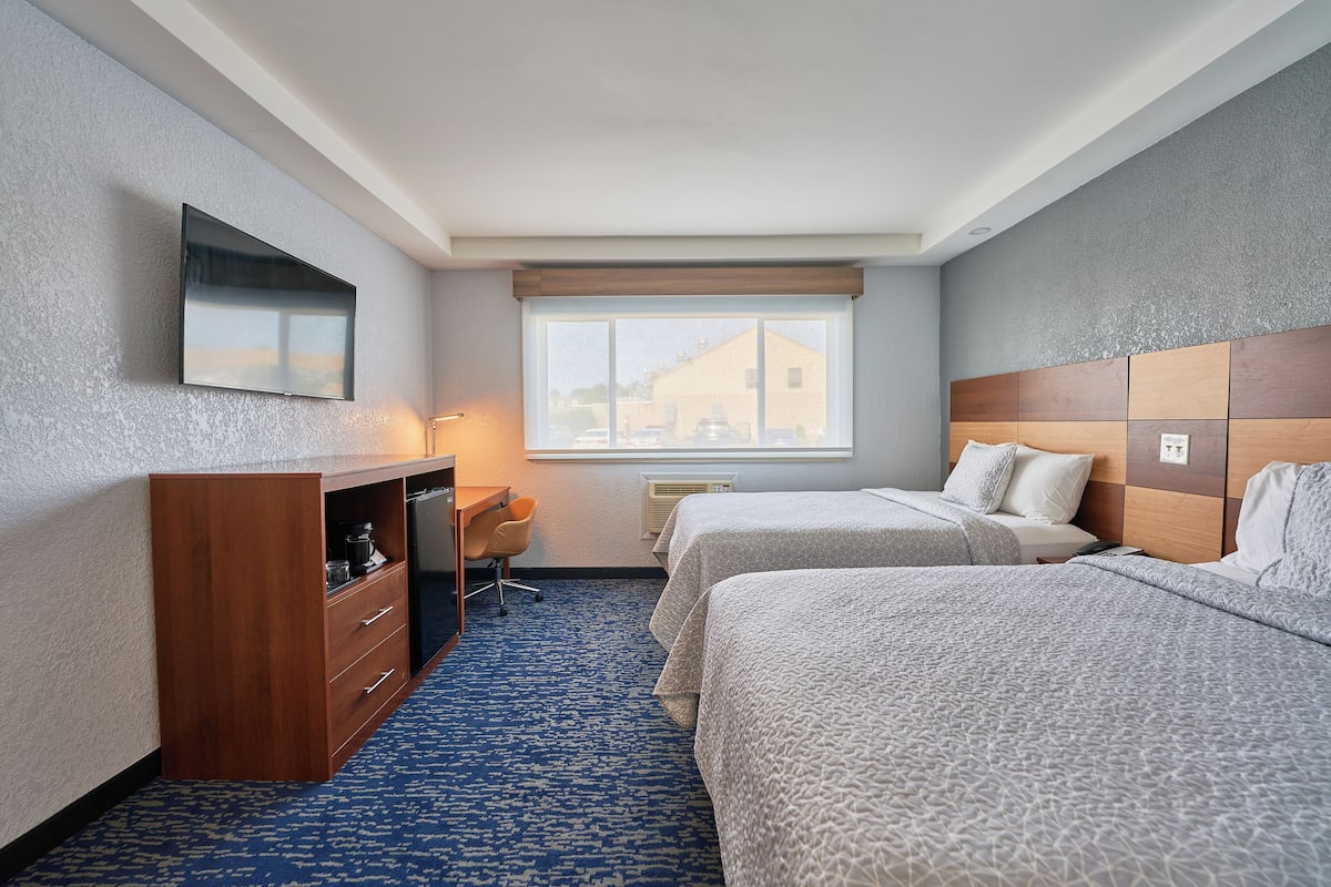 Une chambre d’hôtel avec deux lits, un bureau et un téléviseur fixé au mur.