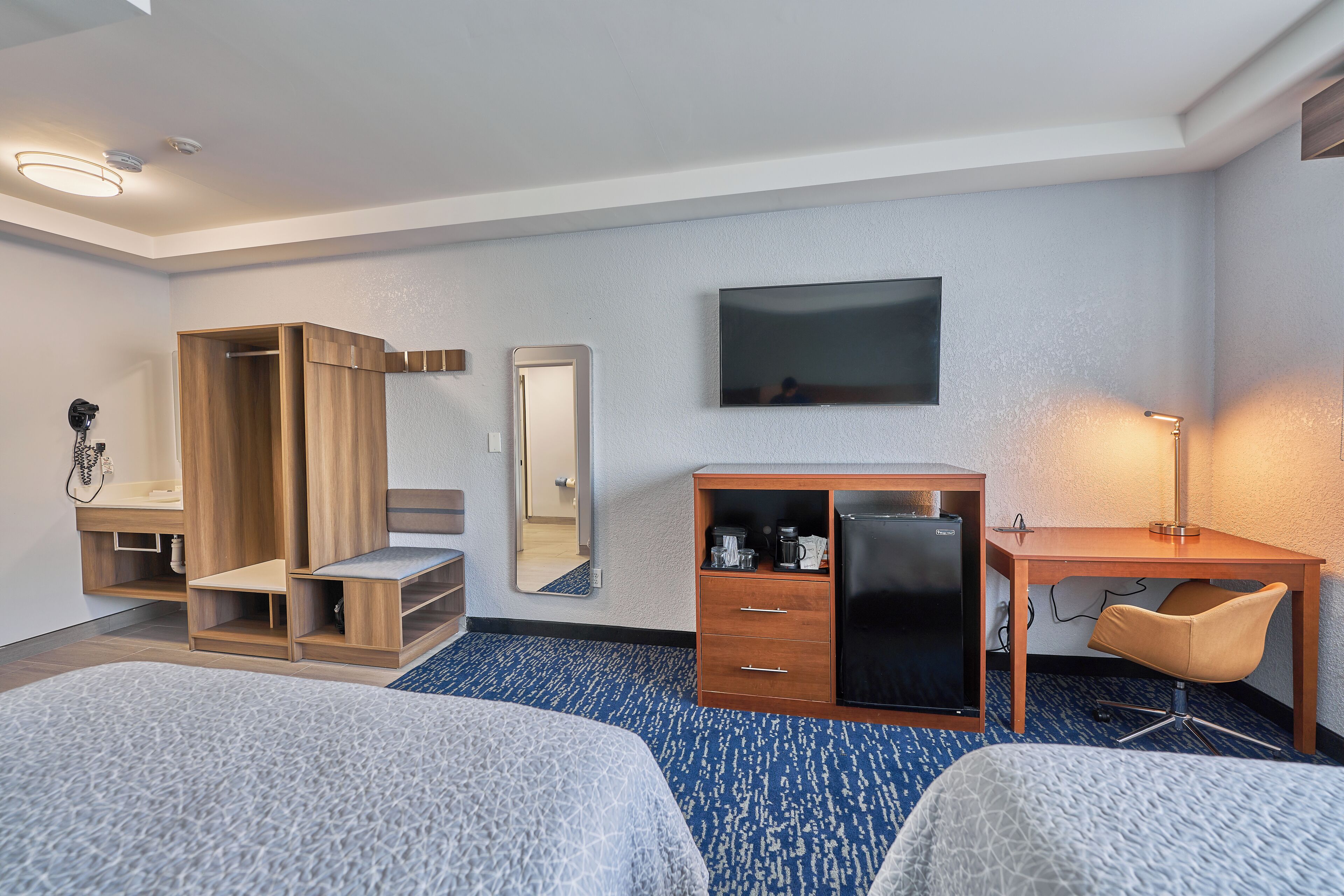 A hotel room with two beds, a desk, a wardrobe, a mirror, and a TV.