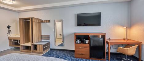 A hotel room with two beds, a desk, a wardrobe, a mirror, and a TV.