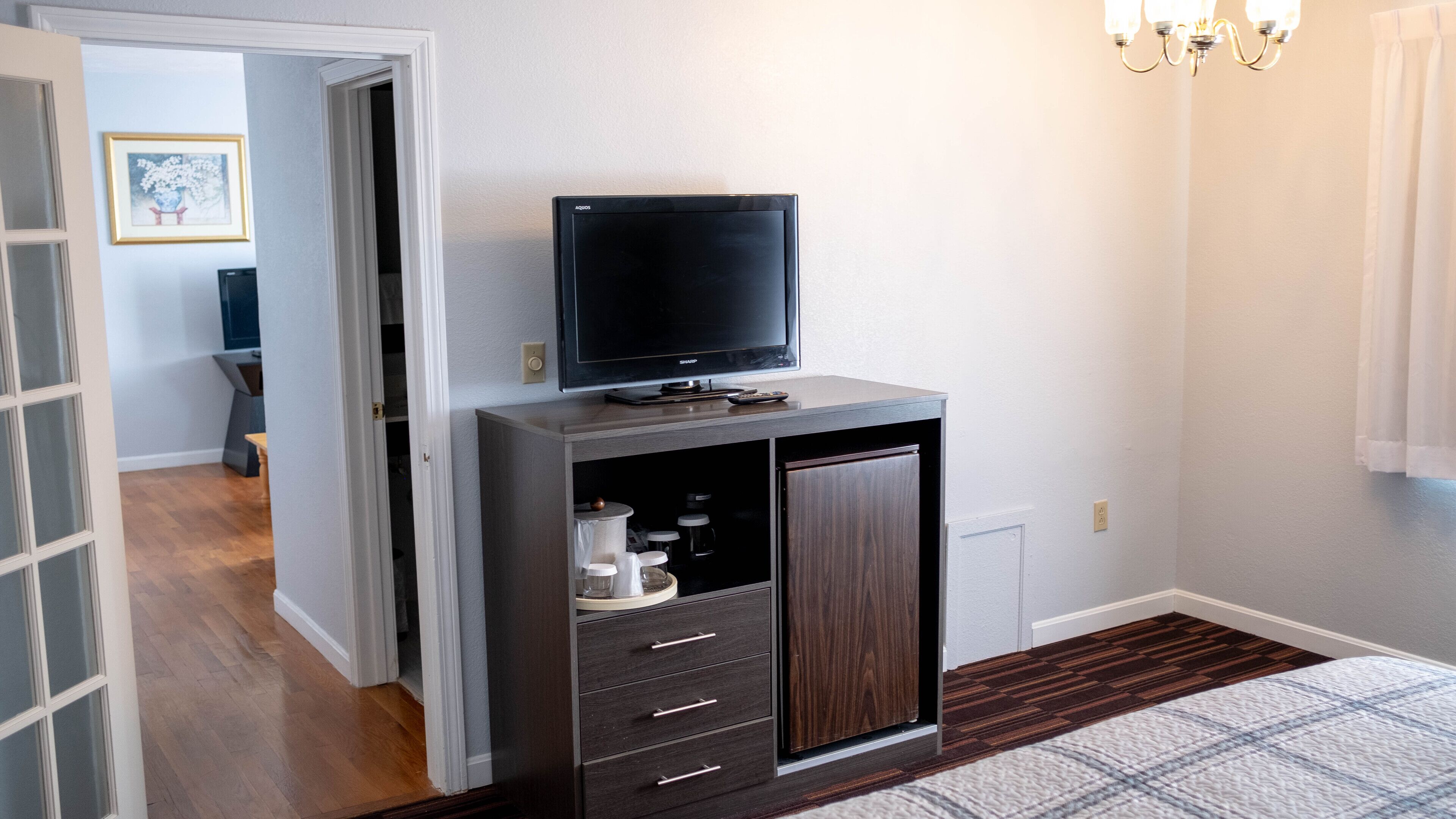 A bedroom with a dark wooden cabinet, a flat-screen TV, and a small refrigerator.