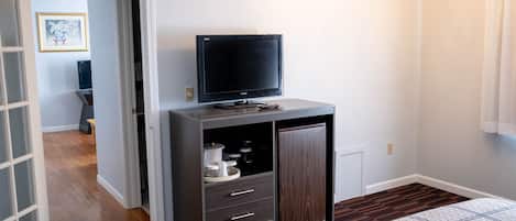 A bedroom with a dark wooden cabinet, a flat-screen TV, and a small refrigerator.