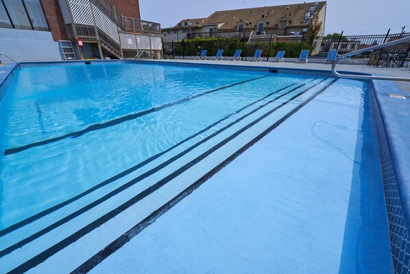 A swimming pool with clear blue water, marked lanes, and sun loungers along the edge.