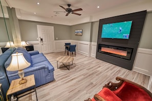 A living room with a blue sofa, a wooden coffee table, a red chair, a television mounted on the wall, and a fireplace.