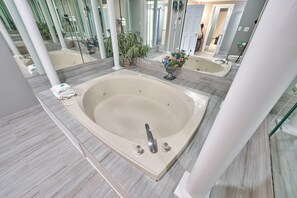 A modern bathroom with a large bathtub, a mirror, and a potted plant.