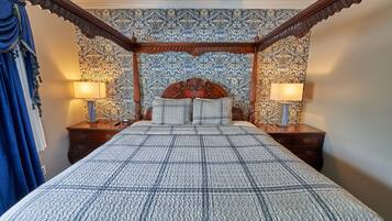 A bedroom with a large bed, ornate headboard, two bedside tables with lamps, and patterned wallpaper.