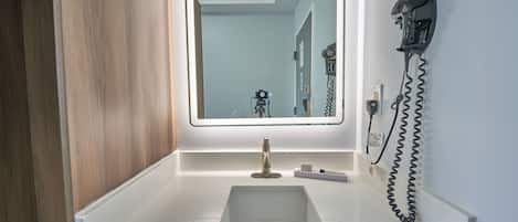 A bathroom with a white sink, a mirror with integrated lighting, and a hairdryer mounted on the wall.