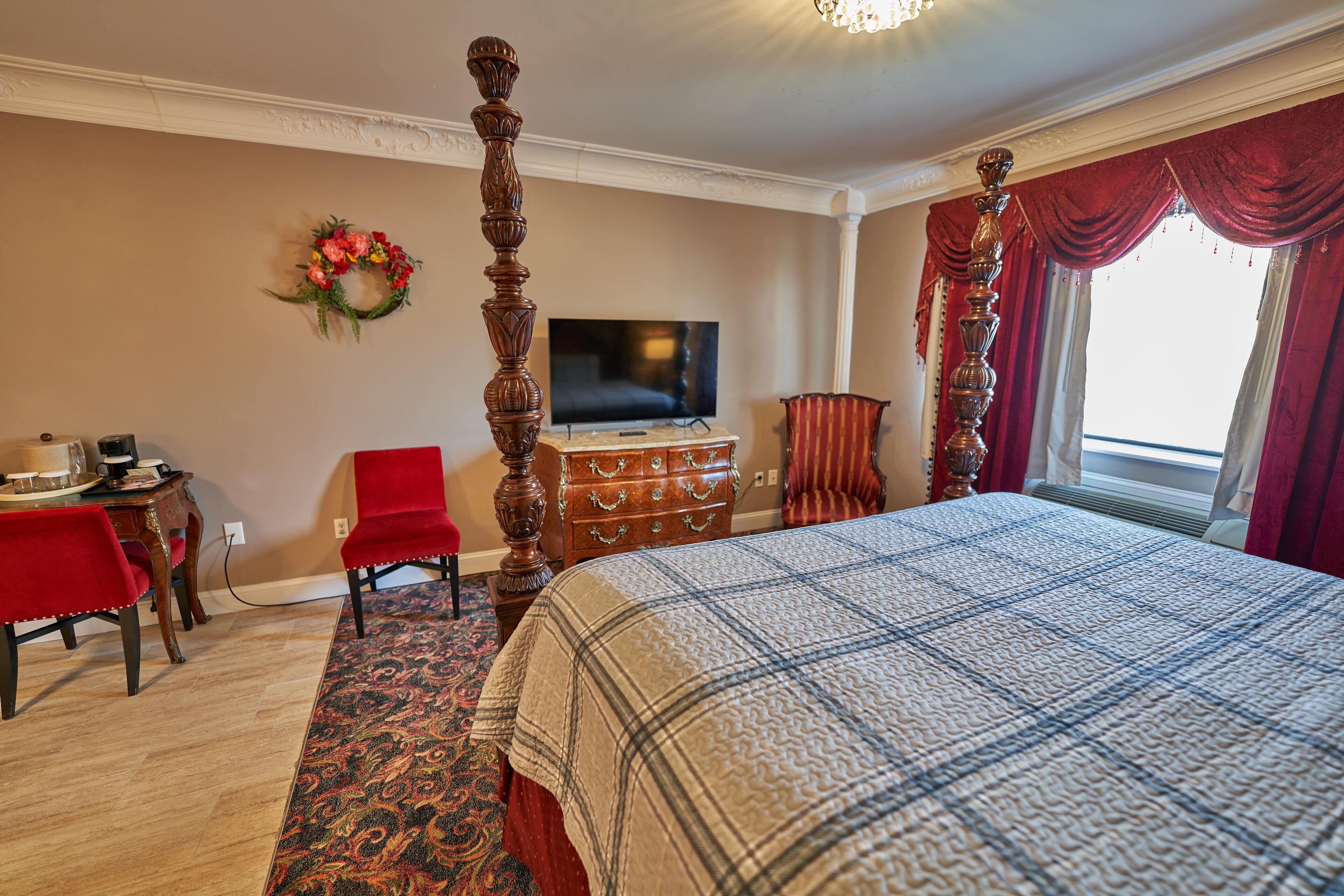 Een slaapkamer met een hemelbed, een televisie, een dressoir en een rode stoel.