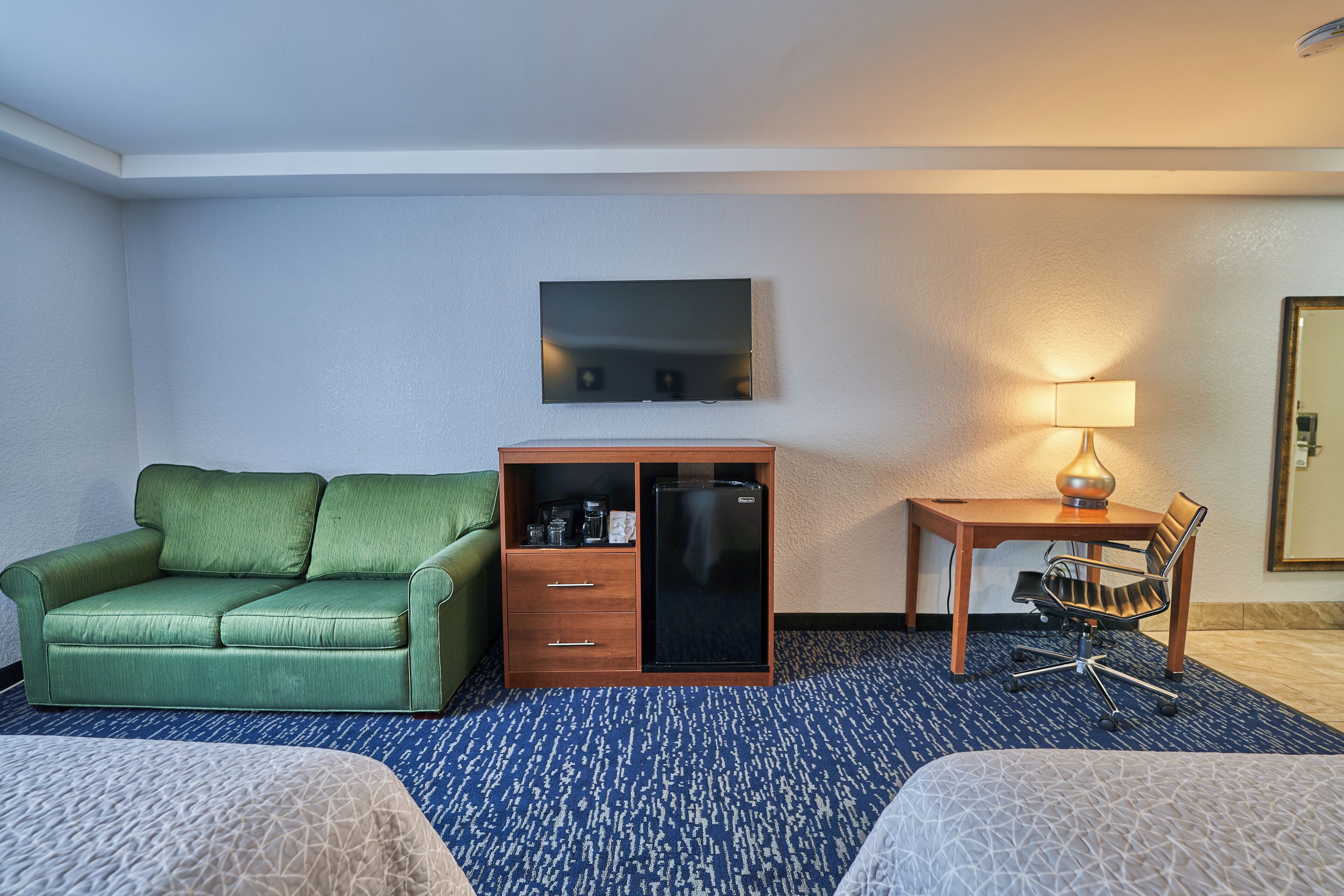 Une chambre d’hôtel avec un canapé vert, un bureau avec une lampe, un téléviseur à écran plat et un mini-bar.
