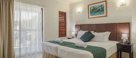 A hotel room with a large bed, a nightstand with a lamp, a painting on the wall, and a window with curtains.