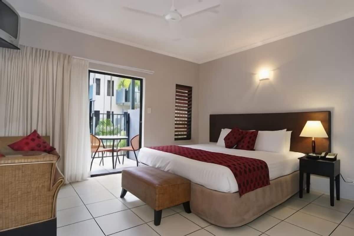 A hotel room with a bed, a chair, a small table, a lamp, and a balcony door.
