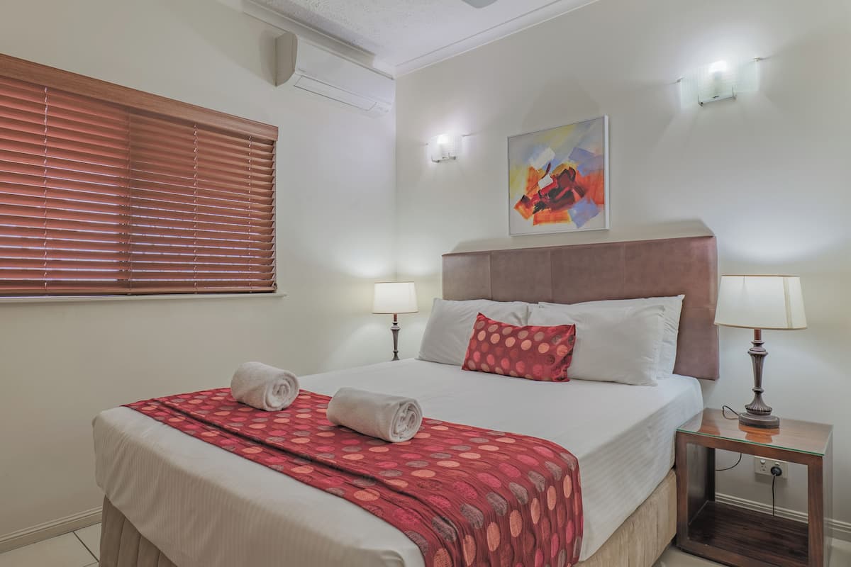 A neatly made bed with a patterned blanket, two bedside lamps, and a painting on the wall.