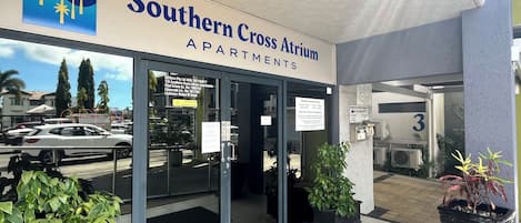 The entrance to Southern Cross Atrium Apartments with a clear view of the parking area and surrounding buildings.