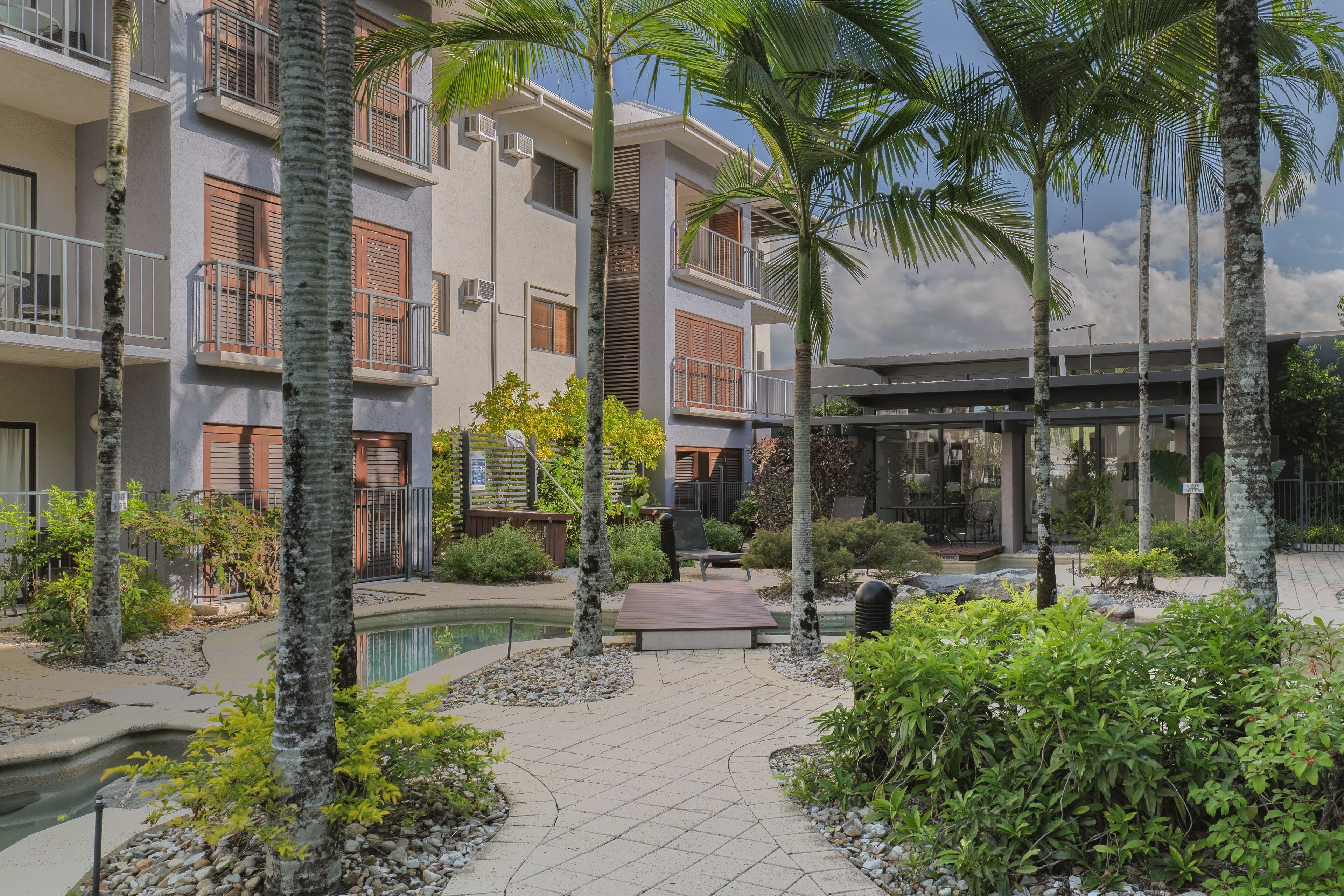 A modern building with multiple balconies, a pool, and lush greenery.