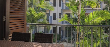 A balcony with wicker furniture, a view of a building with multiple balconies, and lush greenery.