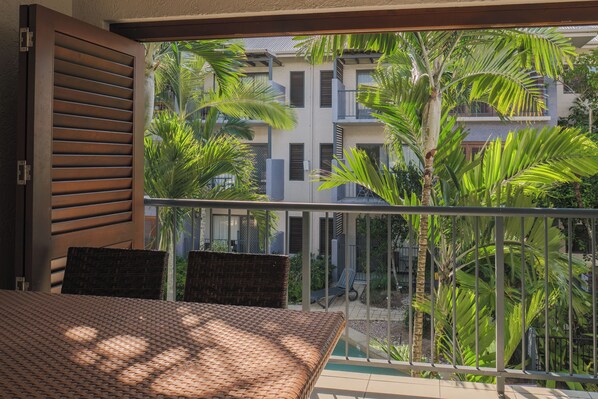 A balcony with wicker furniture, a view of a building with multiple balconies, and lush greenery.