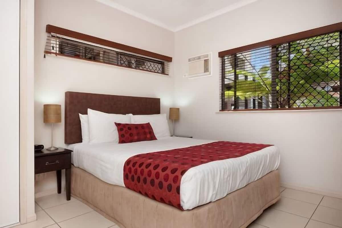 A bedroom with a bed, nightstands, a window with blinds, and a headboard.