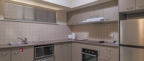 A modern kitchen with stainless steel appliances, beige cabinetry, and a tiled backsplash.