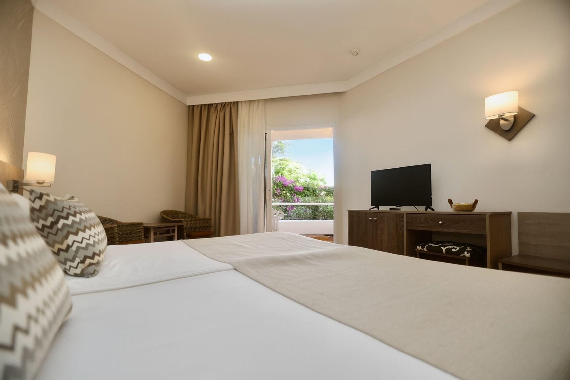 Una habitación de hotel con una cama grande, televisión, una mesita y una silla.