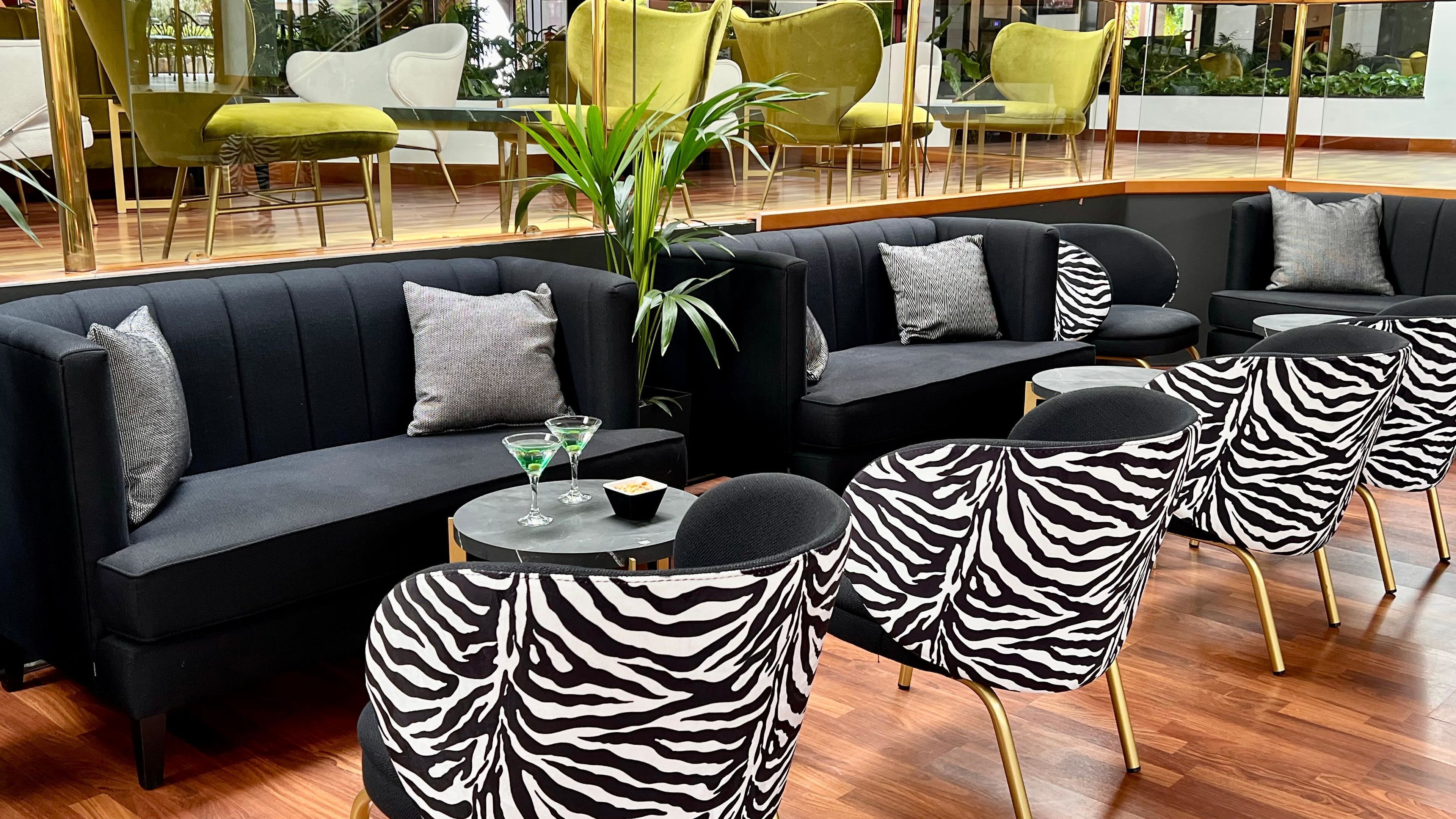 A modern lounge area with a black sectional sofa, zebra-patterned chairs, and a small round table with drinks.