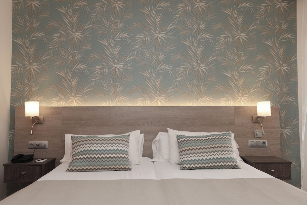 A hotel room with a large bed, two nightstands, and a wall with a leaf pattern.