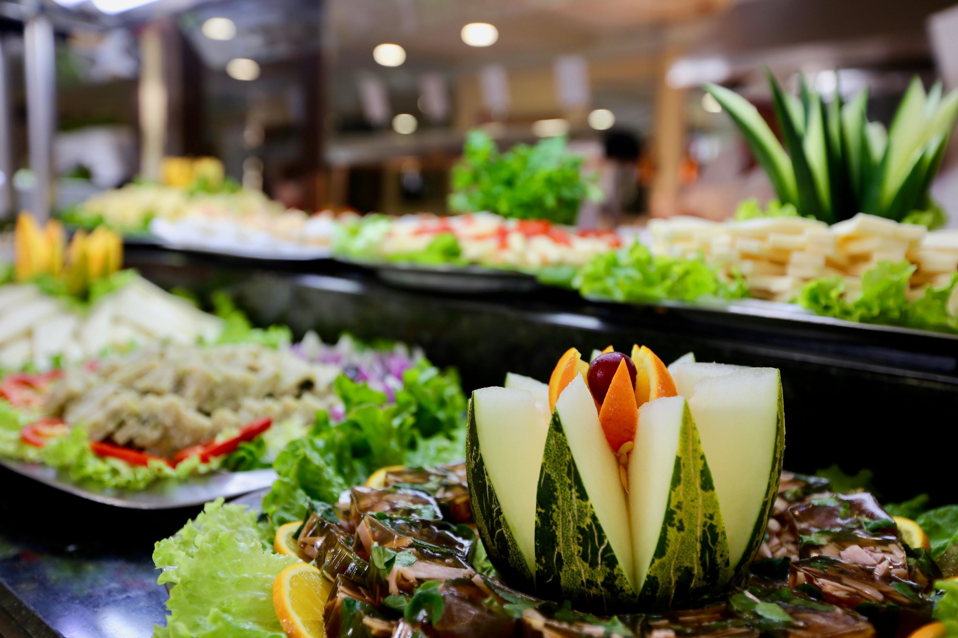 Buffet com diversos pratos, incluindo um arranjo central de legumes e frutas.