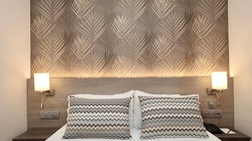 Una cama bien hecha con dos almohadas, un cabecero de madera con motivos de hojas y dos lámparas de noche.